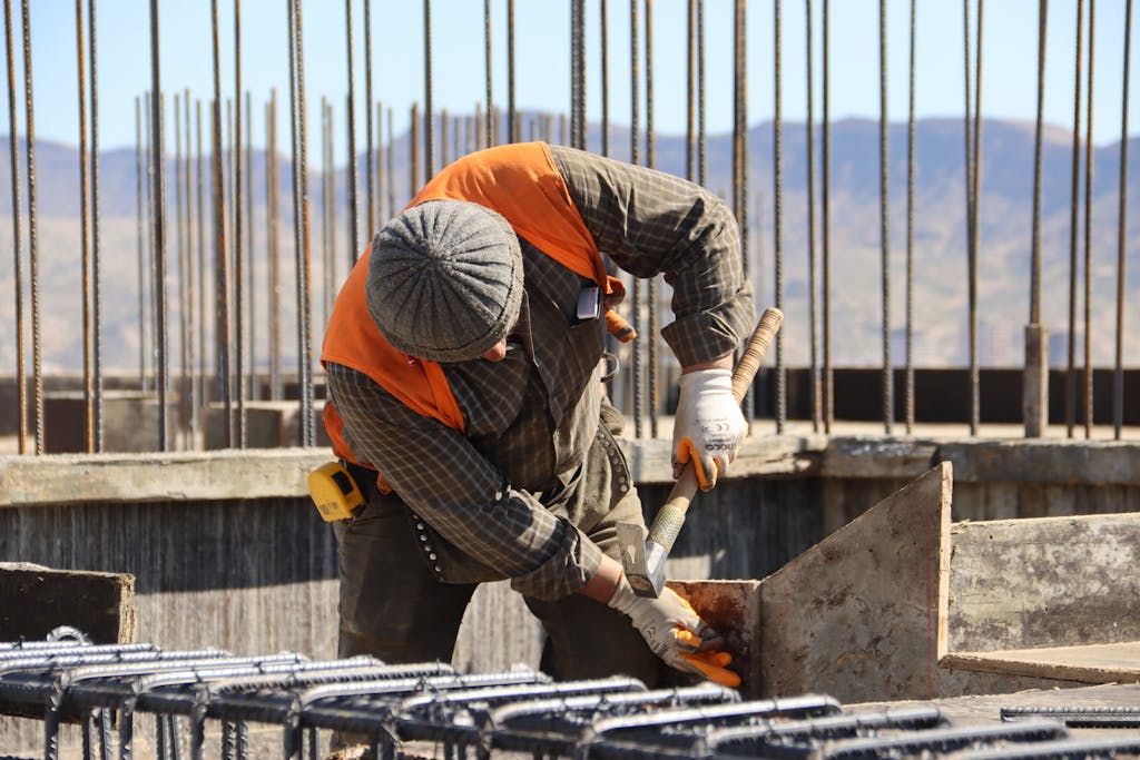 A construction worker in safety gear working at a sunlit site with mountains in background.
