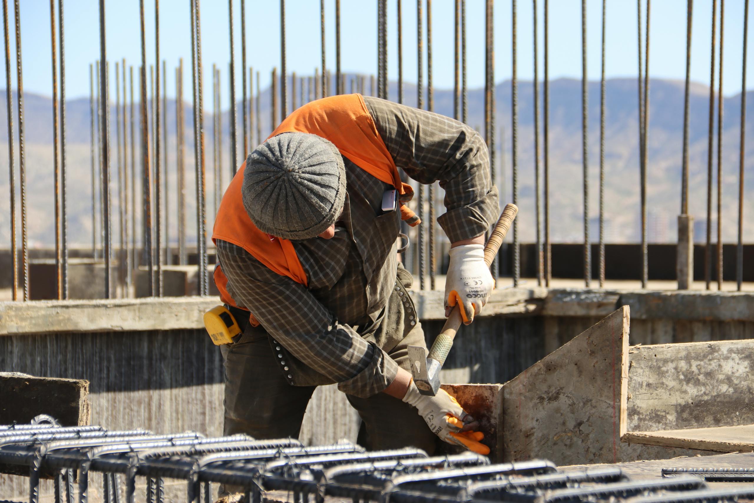 A construction worker in safety gear working at a sunlit site with mountains in background.